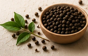 Whole black pepper in a wooden bowl with fresh pepper leaves